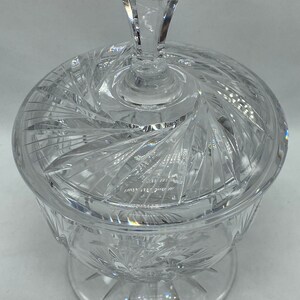 May include: A clear glass candy dish with a lid. The dish has a swirl pattern and a pedestal base. The lid has a diamond-shaped knob.