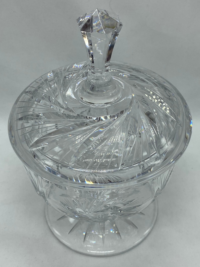 May include: A clear glass candy dish with a lid. The dish has a swirl pattern and a pedestal base. The lid has a diamond-shaped knob.