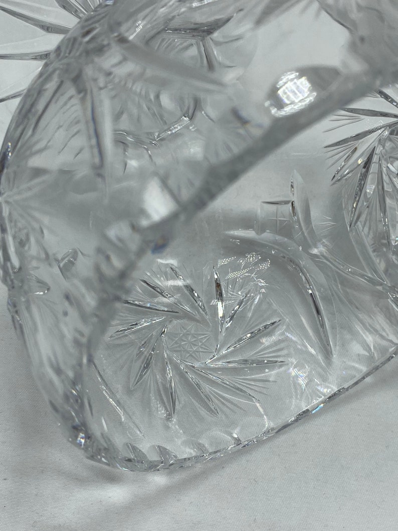 May include: A clear glass bowl with a starburst pattern etched into the bottom. The bowl is made of crystal and has a delicate, elegant design.