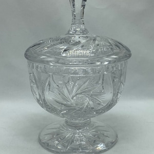 May include: A clear glass candy dish with a lid and a starburst pattern. The dish has a pedestal base.