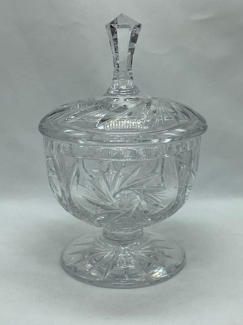 May include: A clear glass candy dish with a lid and a starburst pattern. The dish has a pedestal base.