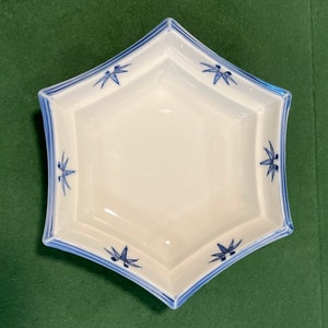 May include: A white ceramic dish with a blue and white bamboo design. The dish is shaped like a star and has a slightly raised rim.