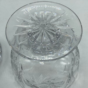 May include: A clear glass bowl with a starburst pattern on the base and a matching lid. The bowl is decorated with a cut glass design.