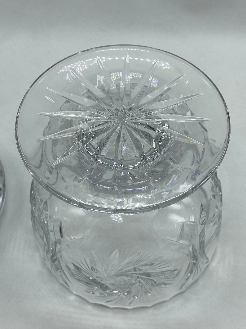 May include: A clear glass bowl with a starburst pattern on the base and a matching lid. The bowl is decorated with a cut glass design.