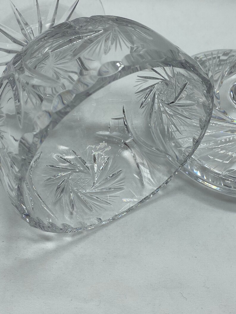 May include: A clear glass cake stand with a cut crystal design. The stand has a round base and a domed top.
