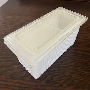 May include: A white rectangular food storage container with a clear, textured lid. The container has vertical ribbed sides and is sitting on a dark brown surface. The lid has the text "FF-453R".