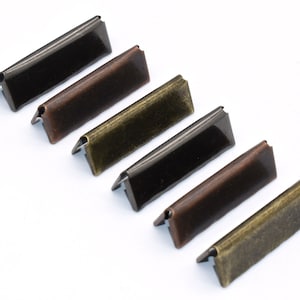 May include: Six metal corner protectors in three different finishes: black, bronze, and antique gold. Each protector has a triangular shape and a smooth, polished surface.