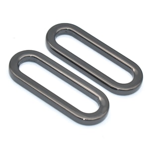 Puede incluir: Dos anillos ovalados de metal negro, cada uno con un borde liso y redondeado. Los anillos son de tamaños ligeramente diferentes y están colocados uno al lado del otro.