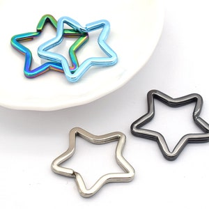 Puede incluir: Tres llaveros con forma de estrella en diferentes colores. Uno es plateado, otro es negro y otro es azul iridiscente.