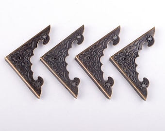 Può includere: Quattro angoli in metallo decorativi con un design floreale. Gli angoli sono di colore bronzo scuro e hanno una finitura anticata.