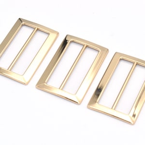 May include: Three gold-toned metal slider buckles. Each buckle has a rectangular shape with a smooth, polished finish.