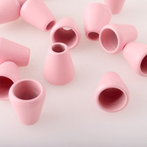 May include: A close-up of pink plastic cord ends. The cord ends are shaped like small cups with a rounded bottom.