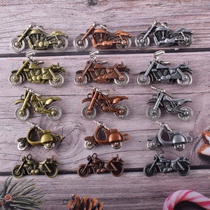 Könnte beinhalten: Eine Sammlung von 15 Miniatur-Motorrad- und Roller-Anhängern in verschiedenen Farben, darunter Silber, Gold, Bronze und Kupfer. Die Anhänger sind in drei Reihen zu fünf auf einer Holzoberfläche angeordnet.