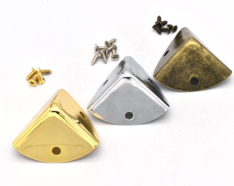 May include: Three corner protectors in gold, silver, and brass finishes. Each protector has a screw hole in the center.