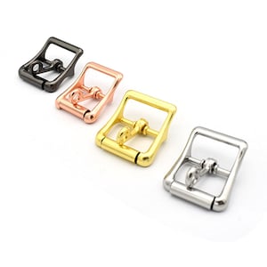 Pode incluir: Quatro fivelas metálicas em diferentes acabamentos: preto, ouro rosa, ouro e prata. Cada fivela é retangular com uma parte superior curva e um pequeno pino redondo de mola.