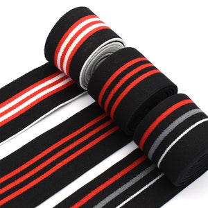 May include: Four rolls of black elastic trim with red and white stripes. The trim is approximately 1 inch wide.