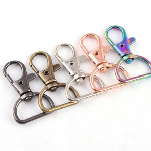 May include: Five metal keychains with different finishes. The keychains are silver, gold, bronze, and iridescent. Each keychain has a swivel hook and a D-ring.