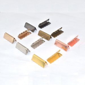 May include: Assortment of metal slider buckles in various finishes, including silver, gold, black, bronze, and rose gold. The buckles are rectangular with a pointed edge and are arranged in rows on a white surface.