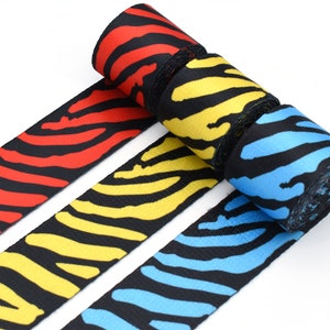 Puede incluir: Tres rollos de cinta de tejido negro y blanco con rayas rojas, amarillas y azules. La cinta es un tejido tejido con una superficie texturizada.