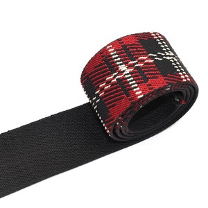 Può includere: Nastrino in tessuto nero e rosso a quadri con un bordo nero intrecciato. Il nastro è arrotolato e il motivo a quadri è visibile.