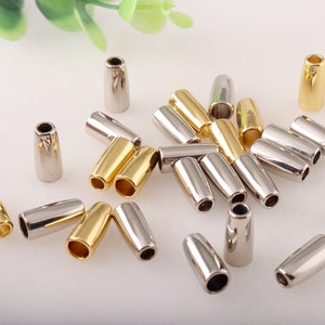 May include: A collection of silver and gold metal cord ends. The cord ends are cylindrical and have a smooth, shiny finish.