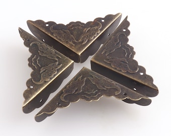 May include: Four antique brass corner protectors with a decorative floral design. Each corner protector has a scalloped edge and a series of small holes.