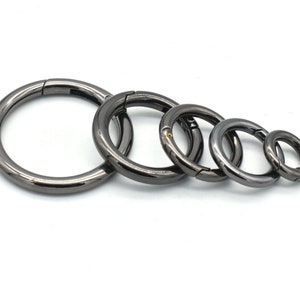 Puede incluir: Cinco llaveros de metal negro de diferentes tamaños. Los anillos están abiertos y tienen un cierre de resorte.