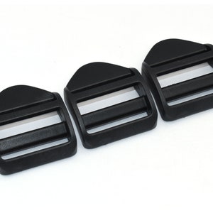 Könnte beinhalten: Drei schwarze Kunststoff-Schiebeschnallen. Die Schnallen sind für die Verwendung mit Gurtband oder Riemen konzipiert.