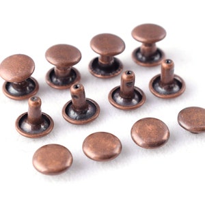 Puede incluir: Una colección de remaches de metal de color cobre, algunos con cabeza elevada y otros con cabeza plana.