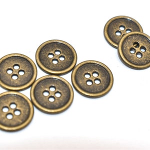 May include: A set of eight antique gold-toned buttons, each with four holes. The buttons are round and have a slightly raised edge.