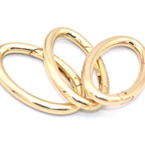 May include: Three gold-colored oval-shaped metal rings with a swivel clasp. The rings are interlocked.