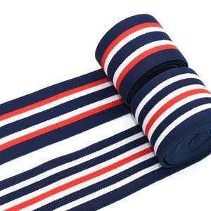 May include: Navy blue elastic trim with white and red stripes. The trim is rolled up and shows the elastic nature of the fabric.