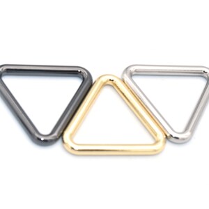 Pode incluir: Três anéis de metal em forma de triângulo em ouro, prata e preto.