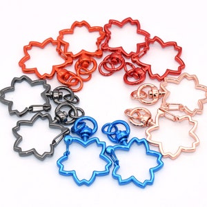 May include: A set of eight metal keyrings in various colours, including silver, gold, blue, and red. Each keyring features a flower-shaped design with a swivel clasp.