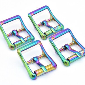 Puede incluir: Cuatro hebillas de cinturón de metal de color arcoíris iridiscente. Las hebillas son de forma cuadrada con un acabado liso.