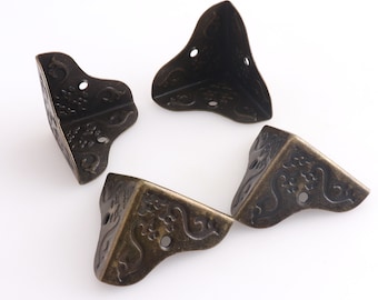 May include: Four antique bronze-colored corner brackets with decorative floral patterns and small holes for screws. The metal corner protectors are designed to reinforce the corners of boxes, chests, or other furniture.