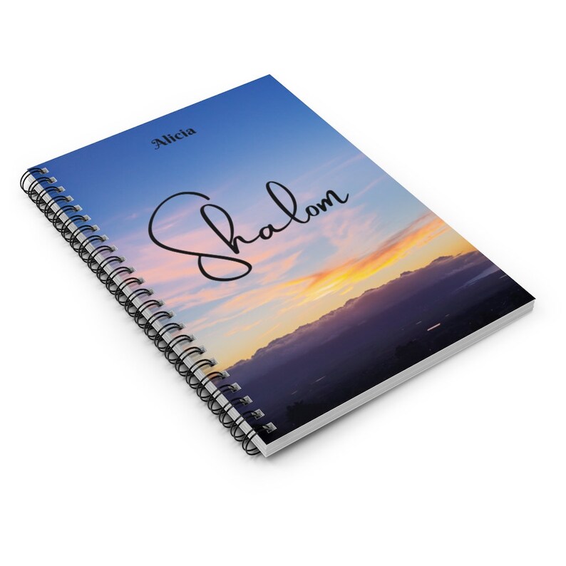 Peut inclure: Un carnet &agrave; spirales avec un fond de ciel de coucher de soleil bleu, rose et orange. Le mot "Shalom" est &eacute;crit en cursive noire sur la couverture. Le nom "Alicia" est imprim&eacute; en noir en haut de la couverture.