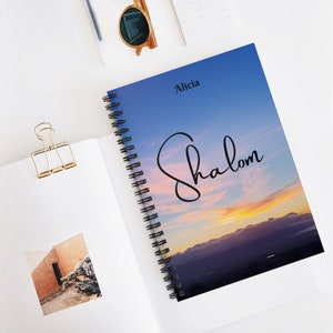 Peut inclure: Un carnet &agrave; spirales avec un fond de ciel de coucher de soleil bleu et violet. Le texte "Alicia Shalom" est &eacute;crit en cursive noire sur la couverture.