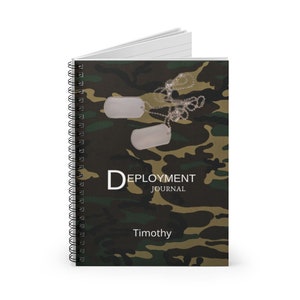 May include: A green, brown, and black camouflage spiral notebook with two silver dog tags and a chain. The notebook has the text "Deployment Journal" and the name "Timothy" printed on the front cover.