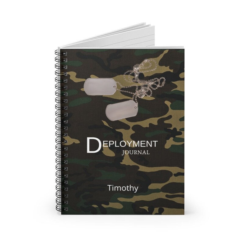 May include: A green, brown, and black camouflage spiral notebook with two silver dog tags and a chain. The notebook has the text "Deployment Journal" and the name "Timothy" printed on the front cover.