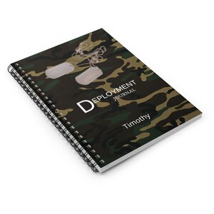 May include: A green, brown, and black camouflage spiral bound notebook with the text "Deployment Journal" and the name "Timothy" printed on the cover. Two silver dog tags are attached to the notebook with a silver chain.