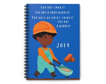 May include: A blue spiral notebook with a cartoon illustration of a young boy wearing an orange hard hat and blue overalls. He is pushing a wheelbarrow with bricks. The text on the notebook reads: "YOU ARE SMART! YOU ARE A HARD WORKER! YOU WILL DO GREAT THINGS! YOU ARE A WINNER! JOEY"
