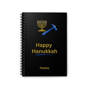 May include: Black spiral notebook with a gold menorah and blue hammer graphic. The text "Happy Hanukkah" is written in gold with a blue underline. The name "Tommy" is written in gold at the bottom.