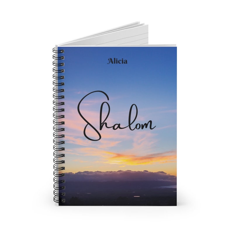 Peut inclure: Un carnet &agrave; spirales avec un fond de ciel de coucher de soleil. Le texte "Shalom" est &eacute;crit en cursive sur la couverture. Le nom "Alicia" est imprim&eacute; en noir en haut de la couverture.