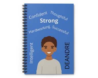 May include: A blue spiral notebook with a cartoon illustration of a smiling boy. The notebook has the words "Strong", "Confident", "Thoughtful", "Hardworking", "Successful", "Intelligent", and "DEANDRE" printed on it.
