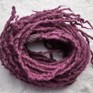 Könnte beinhalten: Ein Bündel tiefvioletter Dreadlocks, kreisförmig gewickelt. Die Dreadlocks haben ein strukturiertes, handgefertigtes Aussehen, wobei sich einige Strähnen nach außen erstrecken. Der Hintergrund ist eine hellgraue, strukturierte Oberfläche.