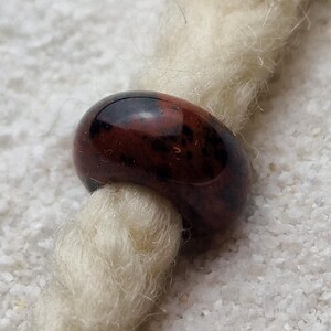 May include: A brown and black glass bead with a mottled pattern. The bead is threaded onto a white cord.