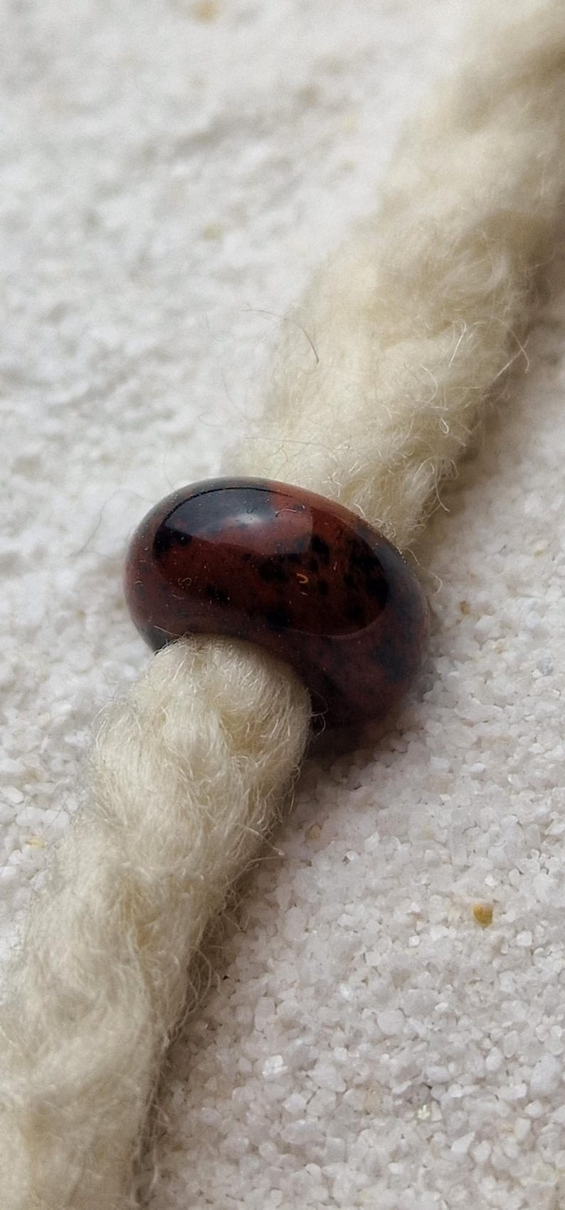 May include: A brown and black glass bead with a mottled pattern. The bead is threaded onto a white cord.