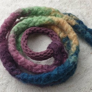 Op de afbeelding: Een close-up van een bundel kleurrijk garen, met tinten groen, blauw, paars en bruin. Het garen is in een spiraalvorm met elkaar verdraaid, waardoor een unieke en textuurrijke look ontstaat.