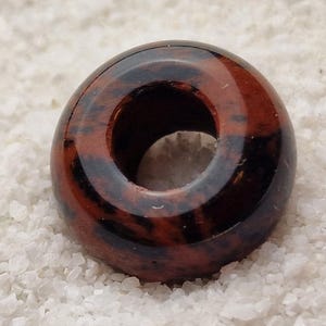 May include: A round, donut-shaped bead made of red and black jasper. The bead has a hole in the center for stringing.